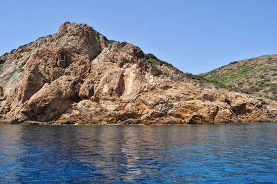 Scenic view of rocks by sea against clear blue sky