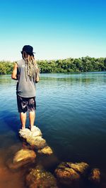 Rear view of man standing on rock in lake against clear sky
