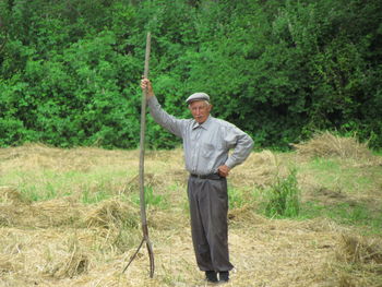 Portrait of senior man with stick standing on grassy field against trees