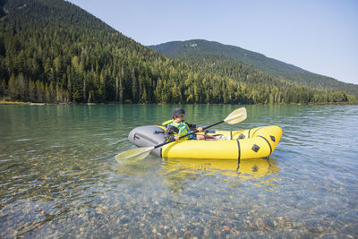 Young boy paddling yellow boat on scenic lake.