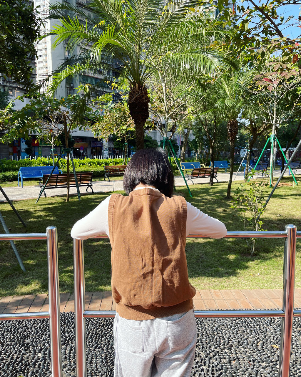 rear view, one person, plant, tree, nature, leisure activity, city, casual clothing, lifestyles, day, park, vacation, women, adult, park - man made space, three quarter length, spring, clothing, public space, outdoors, men, standing, outdoor play equipment, playground, architecture, railing, green, full length