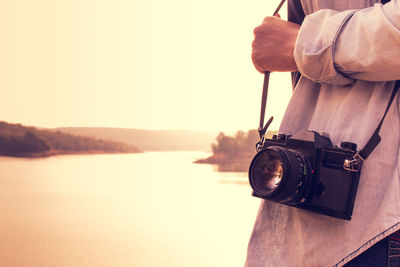 Midsection of woman with camera standing against river