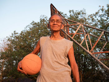 Portrait of man holding basketball while standing outdoors