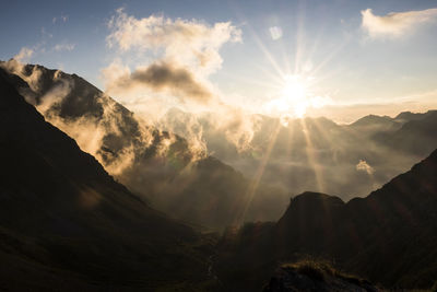 Sunlight streaming through mountains against sky