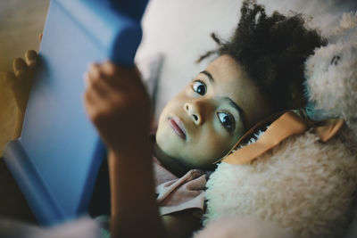 Portrait of boy using digital tablet while lying with teddy bear on bed at home