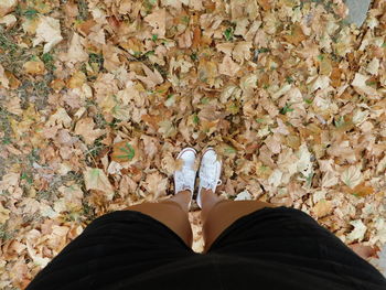 Low section of woman standing on autumn leaves