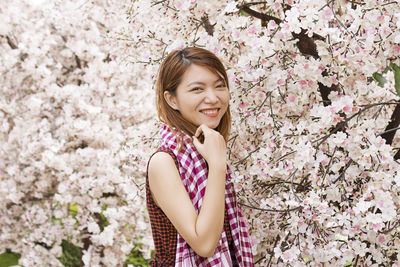 Portrait of smiling woman standing by pink cherry blossom