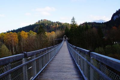 Footbridge amidst trees against sky