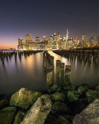 Illuminated buildings in water against sky at night