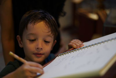 Cute boy writing on book at home