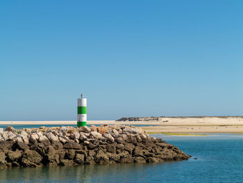 Lighthouse by sea against clear blue sky