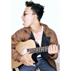 Young man sticking out tongue
 while playing guitar against white background