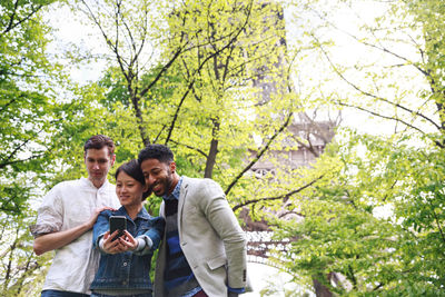 Woman taking selfie with friends sitting against trees in park