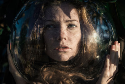 Close-up of young woman wearing glass ball on head against leaves