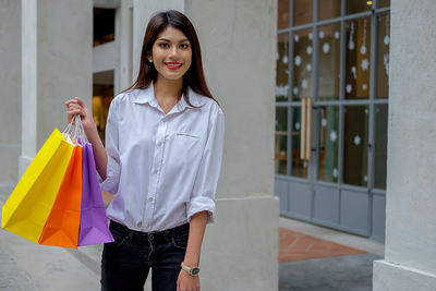 Portrait of smiling woman holding shopping bags in city
