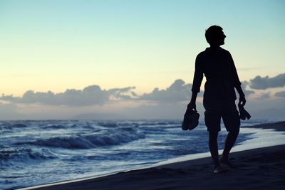 Full length of silhouette man walking on beach against clear sky