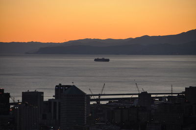 Silhouette city by sea against sky during sunset