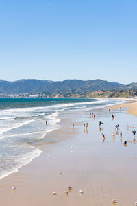 People at beach against clear blue sky