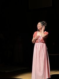 Young asian woman stands in spotlight smiling