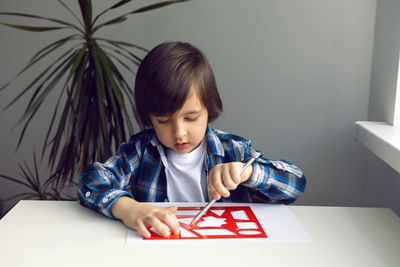 Boy child draws on paper with a ruler on a table sitting by the window