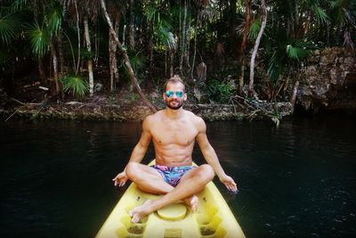 Full length of shirtless man sitting in boat on lake