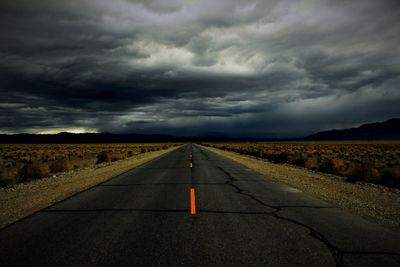 Road passing through field against cloudy sky