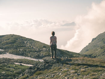 Rear view of female hiker standing on mountain against cloudy sky