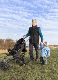 Full length of grandfather with granddaughter standing on grassy field against sky