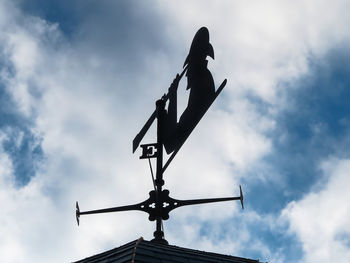 Low angle view of weather vane against cloudy sky
