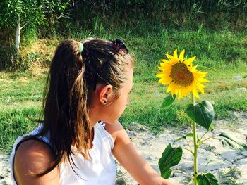 Young woman looking at sunflower blooming on field