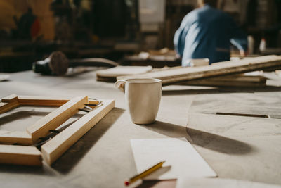 Coffee cup by wooden frame on workbench at repair shop