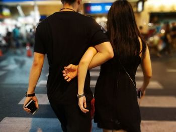 Rear view of couple with arm around walking on street