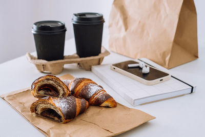 Chocolate croissants with cups of coffee and notepad with smartphone and earphones