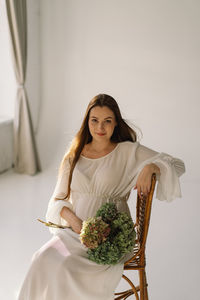 Cute young pregnant girl sitting on the white studio in warm light