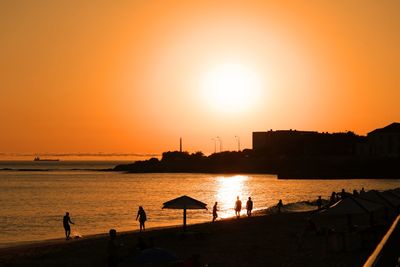 Silhouette people on beach against orange sky