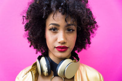 Fashionable young woman with curly hair against pink background