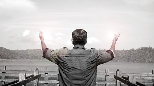 Man with arms raised against sky in black and white.