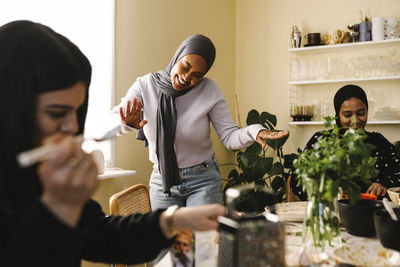 Happy young woman dancing while female friends preparing food at table in kitchen