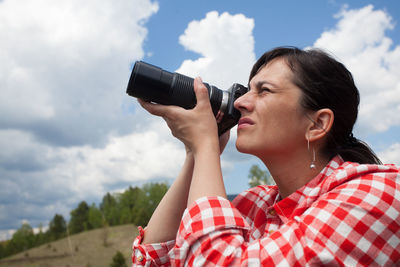 Young woman photographing against sky