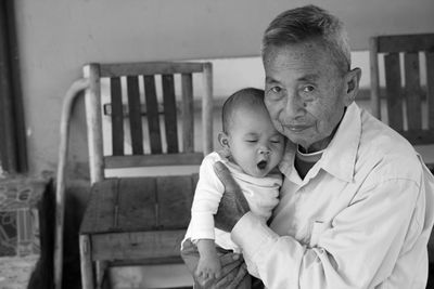 Portrait of grandfather holding grandson against bench