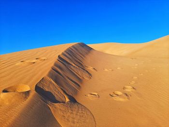 Sand dunes in desert against clear blue sky