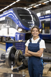 Smiling young trainee standing with arms crossed in warehouse at industry