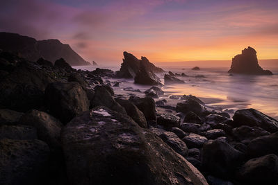 Rocks at seashore against sky during sunset