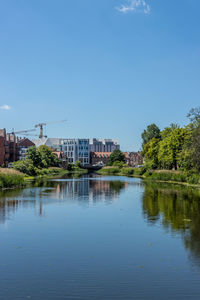 Scenic view of river by buildings against clear blue sky
