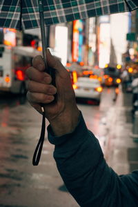 Cropped hand of man holding umbrella on city street during rainy season