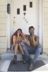 Portrait of young couple sitting at entrance of building