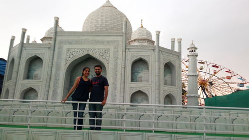 Low angle view of smiling couple standing against taj mahal replica