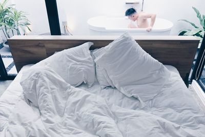 View of man in bathtub behind bed