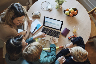 Directly above view of lesbian women planning vacation with sons on laptop at home