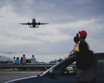 People looking at airplane flying against sky